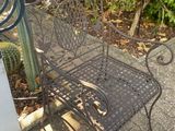 a metal bench sitting on the sidewalk next to a cactus plant