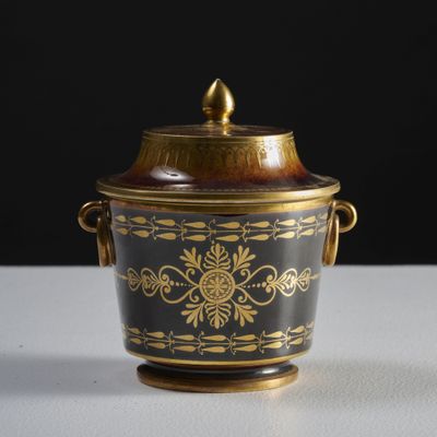 a black and gold vase with a lid on a table