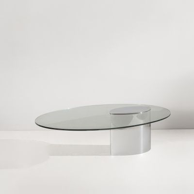 une table basse ovale en verre avec un piètement en métal dans une pièce blanche