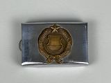 une image représentant une boucle de ceinture en métal sur laquelle est apposé un insigne