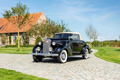 a vintage car parked on a cobblestone road in front of a house