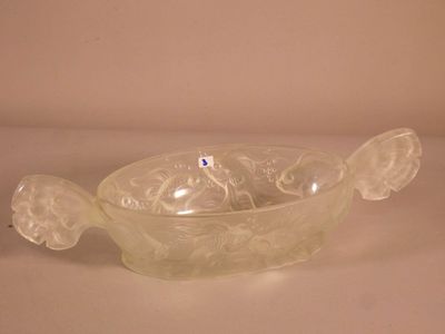 un bol en verre muni d'une anse en forme de poisson, posé sur une table