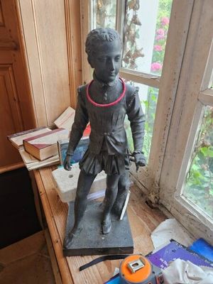 une statue représentant un garçon debout sur un bureau, près d'une fenêtre
