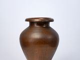 un petit vase marron posé sur une table blanche