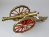 a brass cannon on a red wheel on a white surface