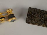pair of gold plated binoculars next to a wallet on a white surface