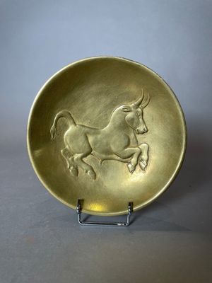 assiette en or décorée d'un cheval, posée sur un socle en métal