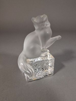une figurine en verre représentant un chat assis sur une boîte