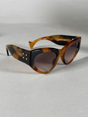 une paire de lunettes de soleil à monture écaille posée sur une surface blanche, sur fond blanc