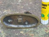 un flacon de colle posé à côté d'un objet en bronze