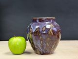 a green apple next to a brown vase on a table
