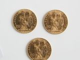 Trois pièces d'or sont représentées sur une surface blanche, à côté d'une paire de ciseaux