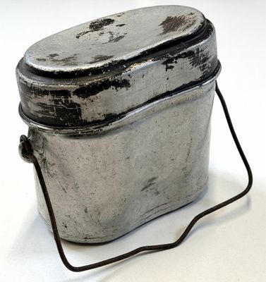 un petit récipient en métal muni d'une poignée, posé sur une surface blanche