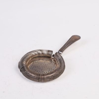 une assiette en argent sur laquelle repose une cuillère, posée sur un fond blanc