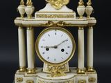 une horloge blanche et dorée posée sur un socle en marbre