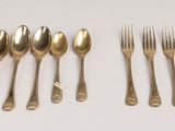 six forks and six spoons are lined up on a white surface