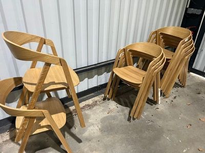 Plusieurs chaises en bois sont alignées contre un mur devant un bâtiment.