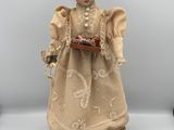 une poupée ancienne représentant une femme en robe et chapeau, tenant un panier de fleurs