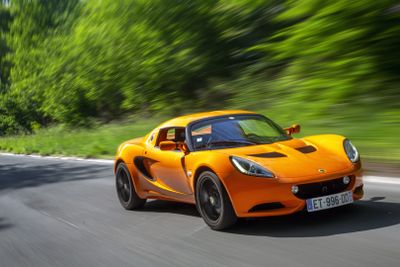 an orange sports car driving down a road with trees in the background
