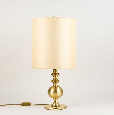 une lampe de table dorée avec un abat-jour beige sur fond blanc