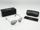 Des lunettes de soleil Chanel et leur étui posés sur une surface blanche, avec une boîte noire