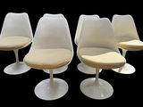 four white tulip chairs with beige cushions on a black background