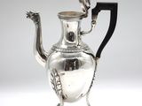 an antique silver tea pot with a black handle on a stand