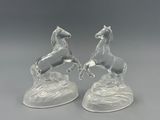 paire de figurines de chevaux en verre transparent posées sur un rocher