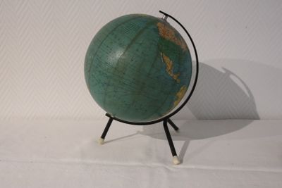 un petit globe vert posé sur un socle, sur une surface blanche