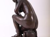 statue of a man sitting on a wooden base with his hands on his knees