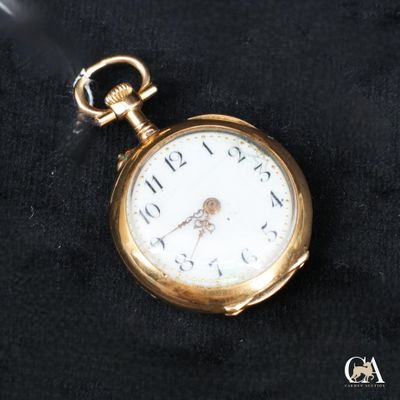 une petite montre de poche en or posée sur un tissu noir