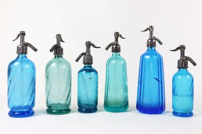 six bouteilles en verre bleues sont alignées sur une surface blanche