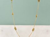 un collier plaqué or orné de quatre petites perles, posé sur une surface en marbre