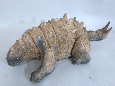 une petite statue représentant un dinosaure posée sur une surface blanche