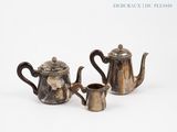 two silver teapots and a coffee pot on a white surface