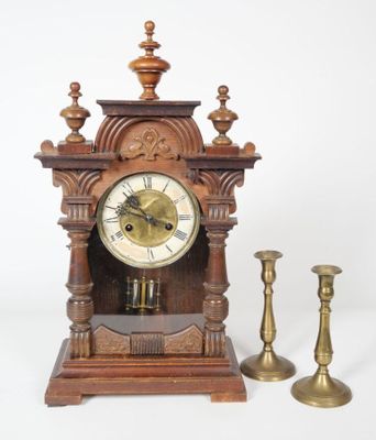 a small wooden clock and two candles on a white background