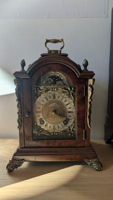 une petite horloge en bois posée sur une table à côté d'une lampe