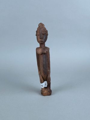 une vieille statue en bois représentant une personne, avec une étiquette accrochée à son cou