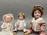 trois poupées en porcelaine assises côte à côte sur une table