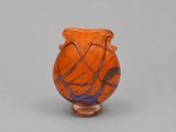 un vase orange posé sur une table blanche, près d'un mur gris