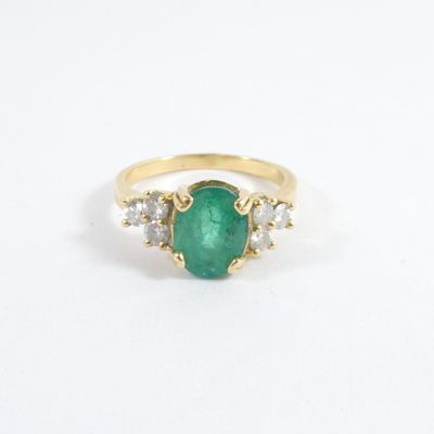 un gros plan d'une bague en or sertie d'une pierre verte et de deux diamants blancs