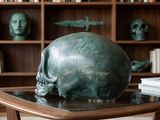 a bronze skull sitting on a table in front of a bookshelf