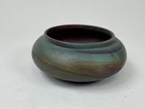 un vase vert et violet posé sur une surface blanche