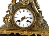 a gold clock with a statue of a man sitting on top of it