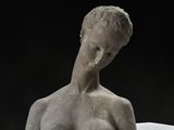 sculpture représentant un torse féminin sur un socle blanc, avec un fond noir