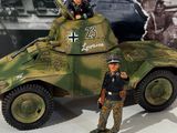two figurines of men standing in front of a toy tank