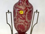 un vase rouge posé sur un socle, sur lequel est collé un autocollant jaune