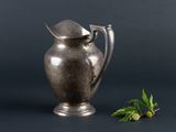 an old silver pitcher next to a sprig of mint on a black background