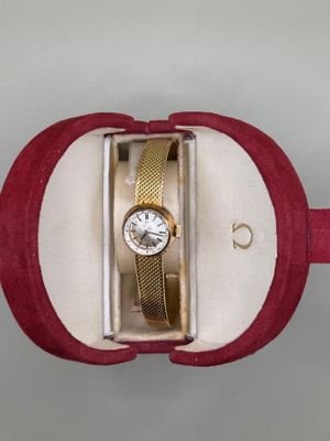 une montre dans un coffret rouge, avec un bracelet doré