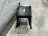 a black stool sitting on the floor next to a gray couch